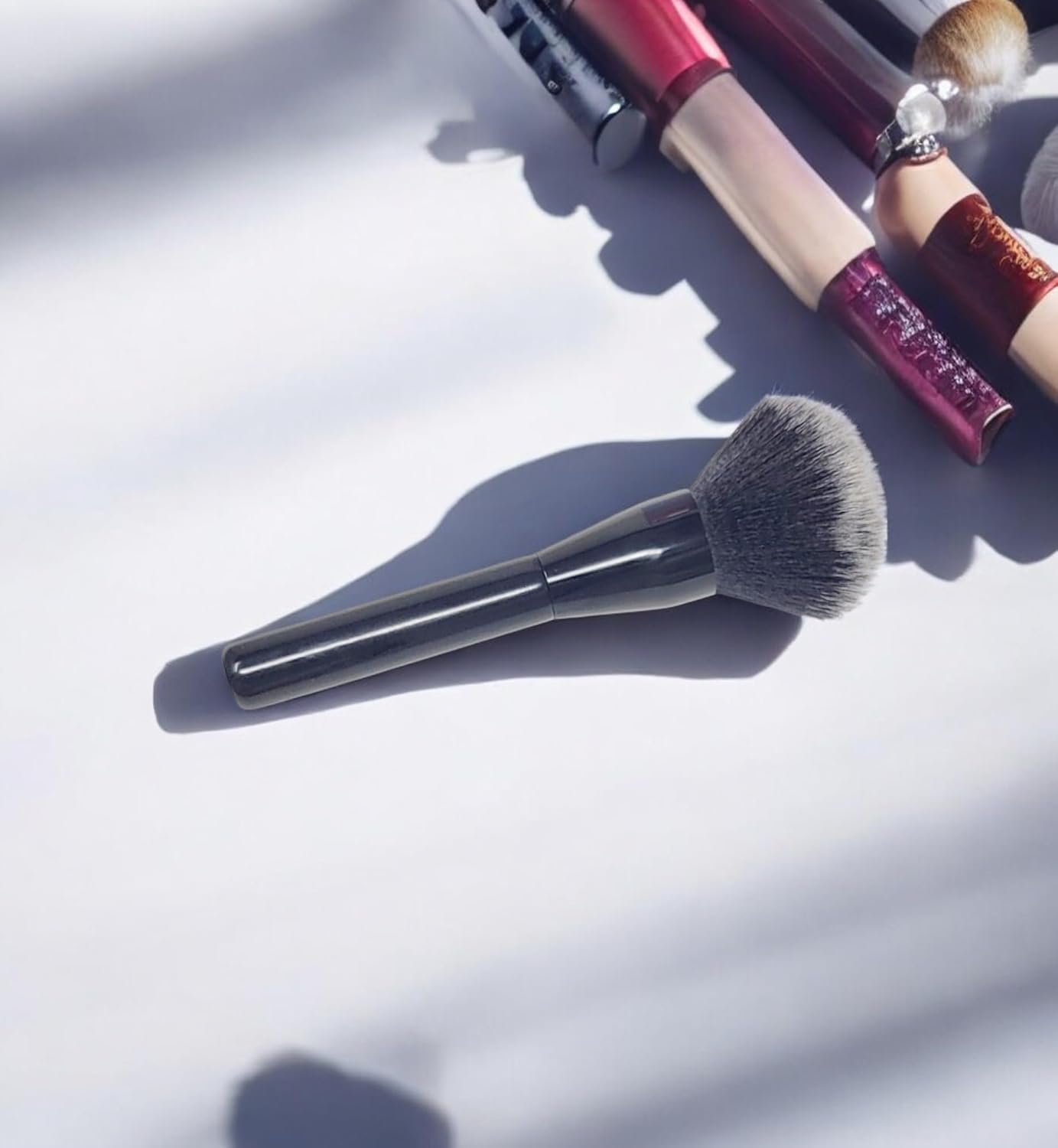 Triangular-shaped kabuki brush with a long, glossy black handle. Featuring fluffy and soft bristles, ideal for applying bronzer, setting powder, and loose powder on both the face and body.